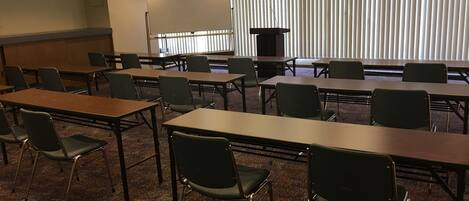 A conference room with multiple tables and chairs, a podium, and a projection screen.