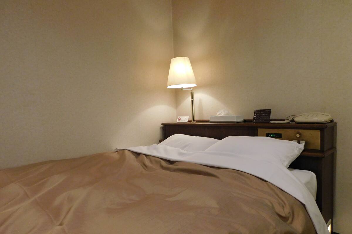 A hotel room with a bed, a bedside lamp, a telephone, and a digital clock on the nightstand.