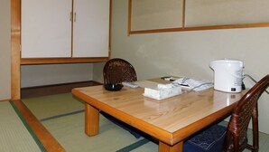 A traditional Japanese room with tatami flooring, a wooden table, a white electric kettle, and a woven chair. - Hotel Crown Hills Kitami (Kitami)