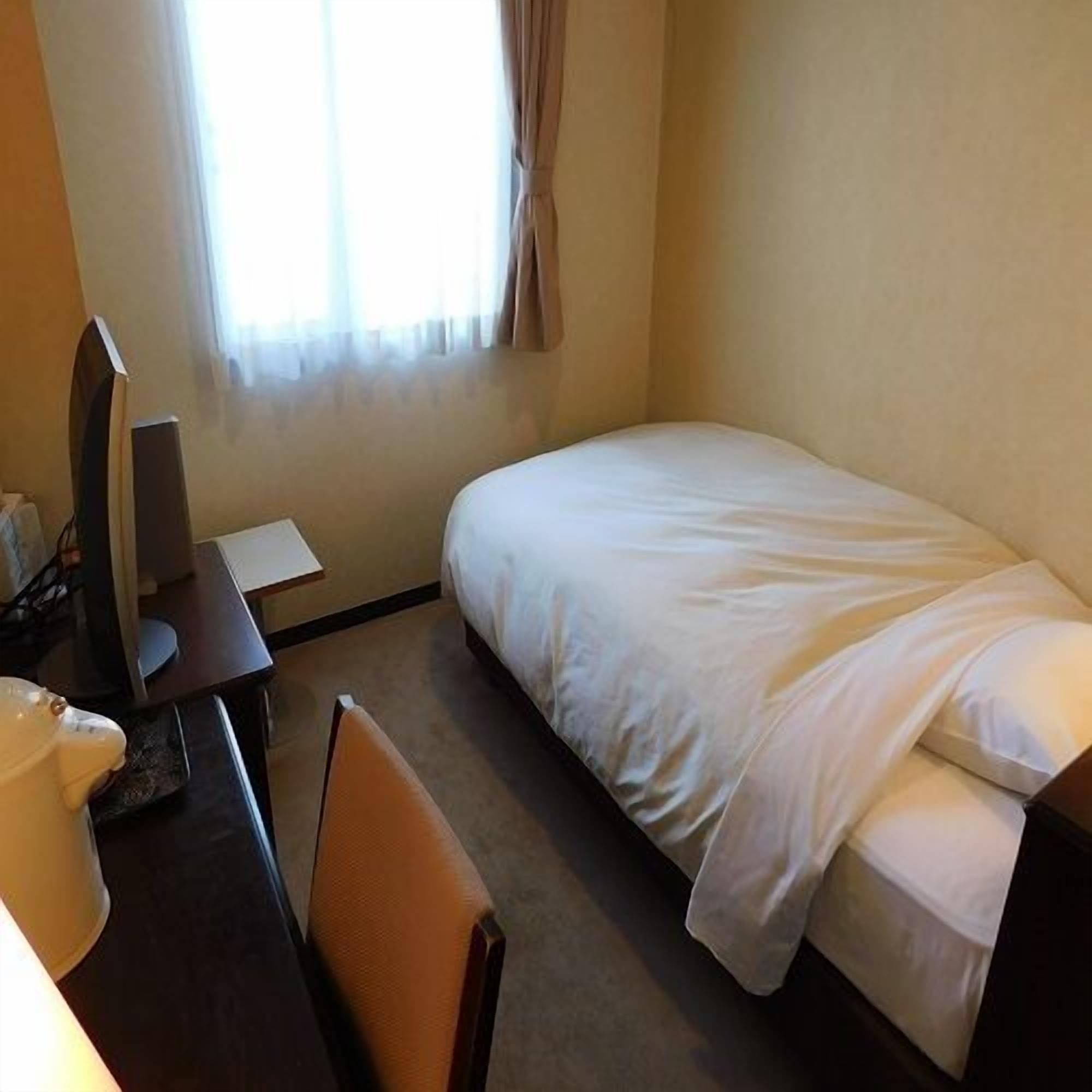 Une chambre d’hôtel avec un lit, un bureau, une chaise, une télévision et une fenêtre avec des rideaux.