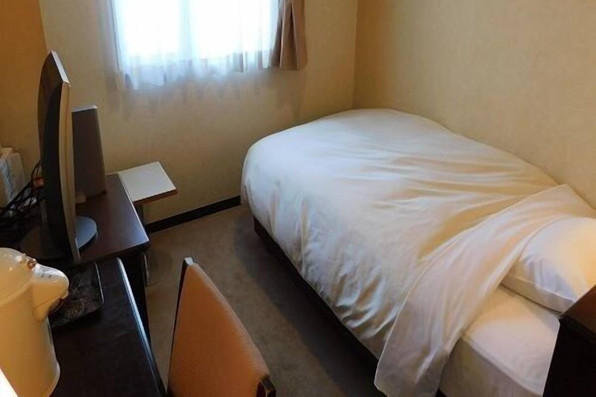 A hotel room with a bed, a desk, a chair, a TV, and a window with curtains.