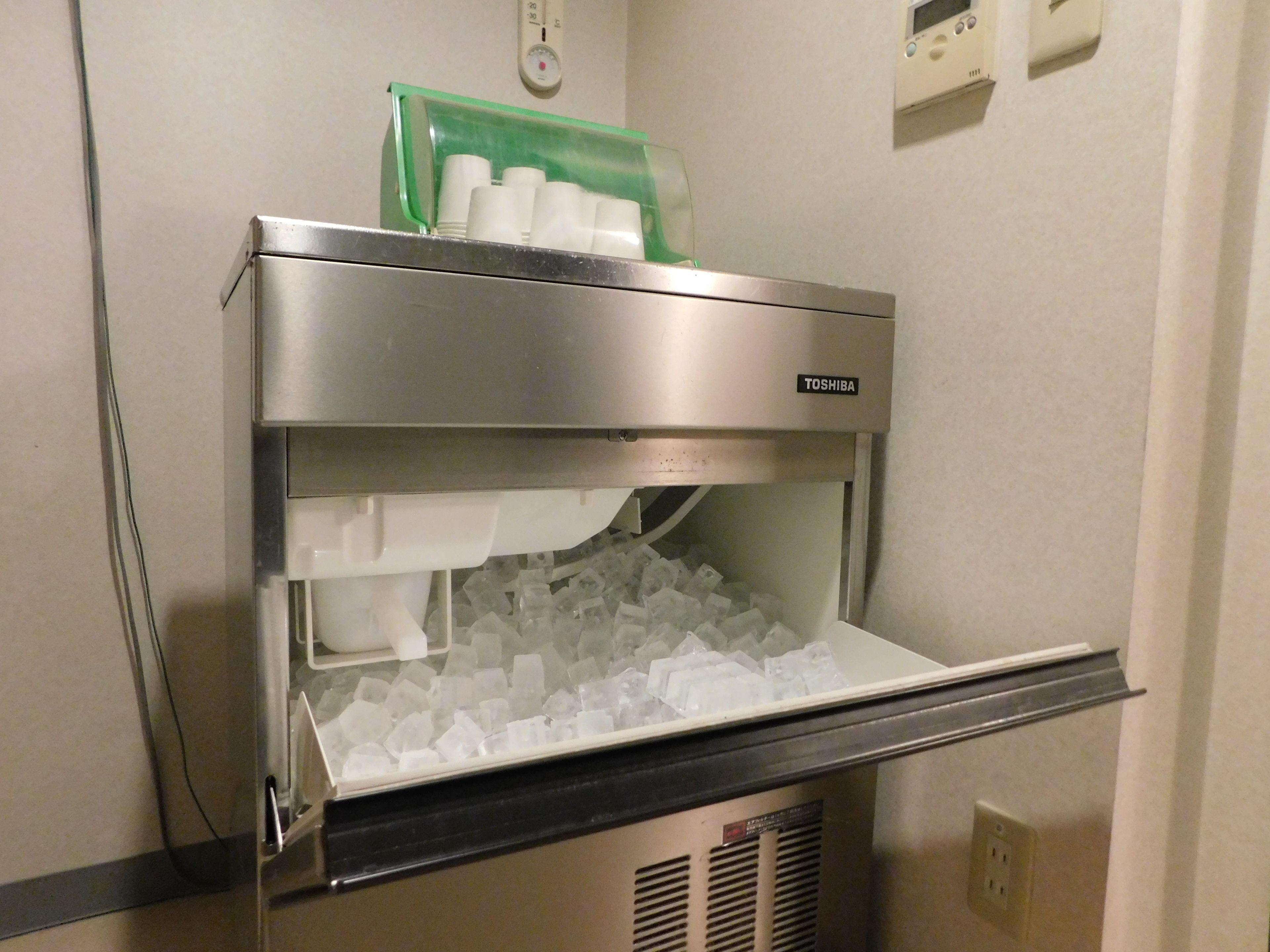A Toshiba branded ice dispenser with a green cup holder and a tray of ice cubes.