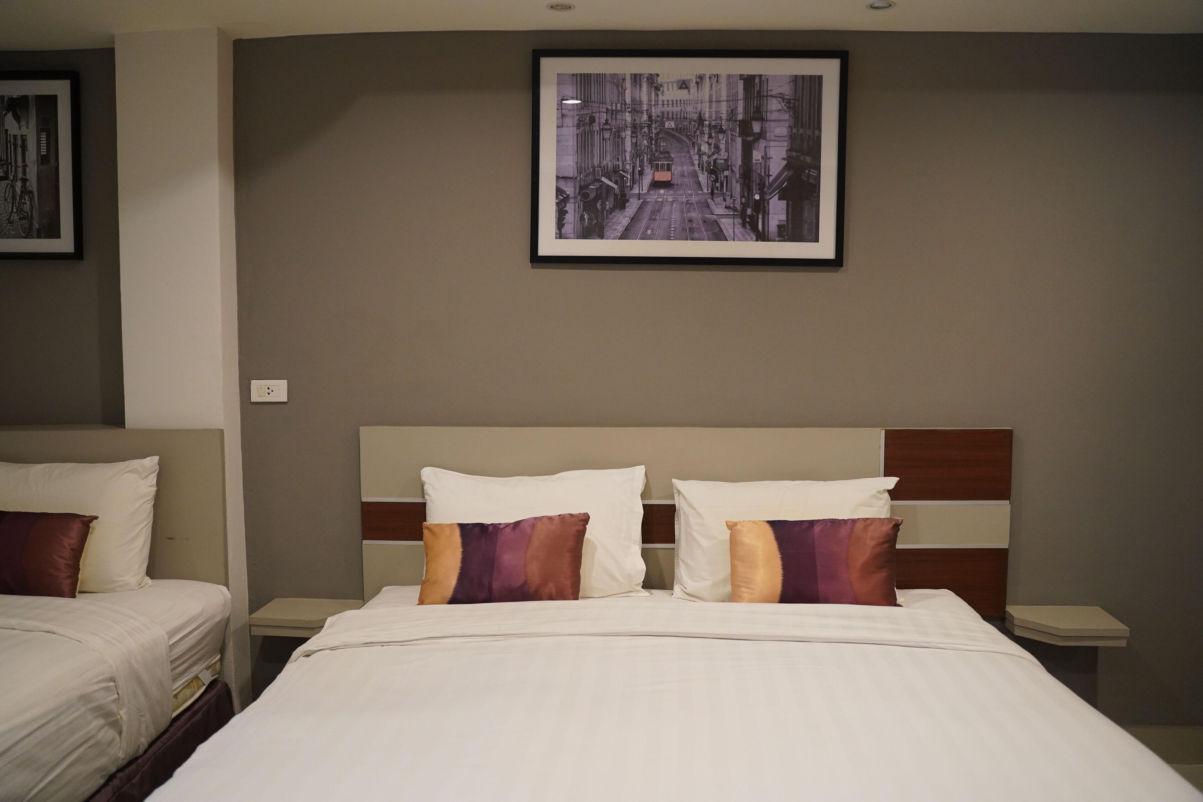 A hotel room with two beds, a large framed picture on the wall, and a nightstand with a lamp.