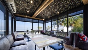 A modern interior with a large table, seating, and large windows overlooking a scenic view. - The Loft Seaside Sriracha (Si Racha)