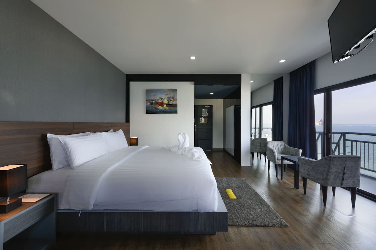A modern hotel room with a large bed, a painting on the wall, a balcony with a view, and a seating area with a table.