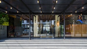 A modern hotel entrance with glass doors, a visible seating area, and a logo on the right. - The Loft Seaside Sriracha (Si Racha)