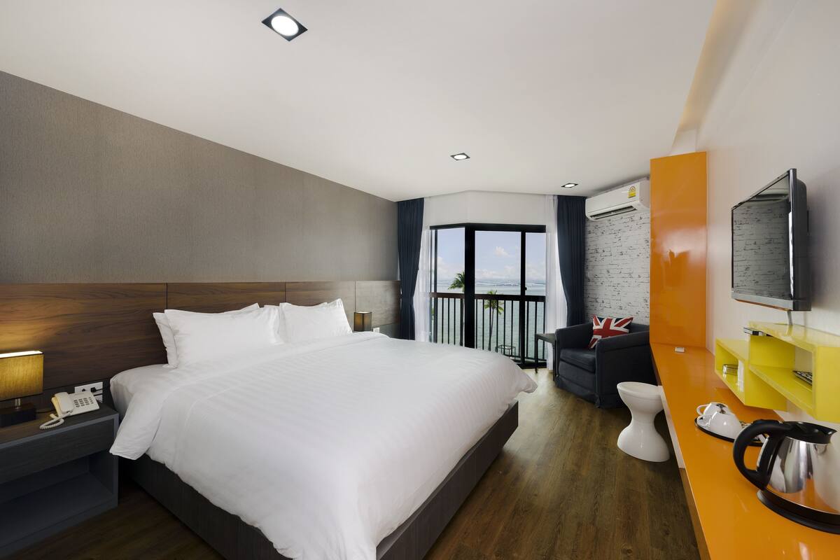 A hotel room with a large bed, a bedside telephone, a small table with a lamp, a sofa, a toilet, and a television.