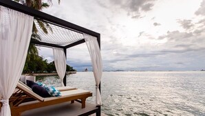 A wooden deck with a single lounge chair and a canopy, overlooking a body of water with a distant shoreline and palm trees. - The Loft Seaside Sriracha (Si Racha)