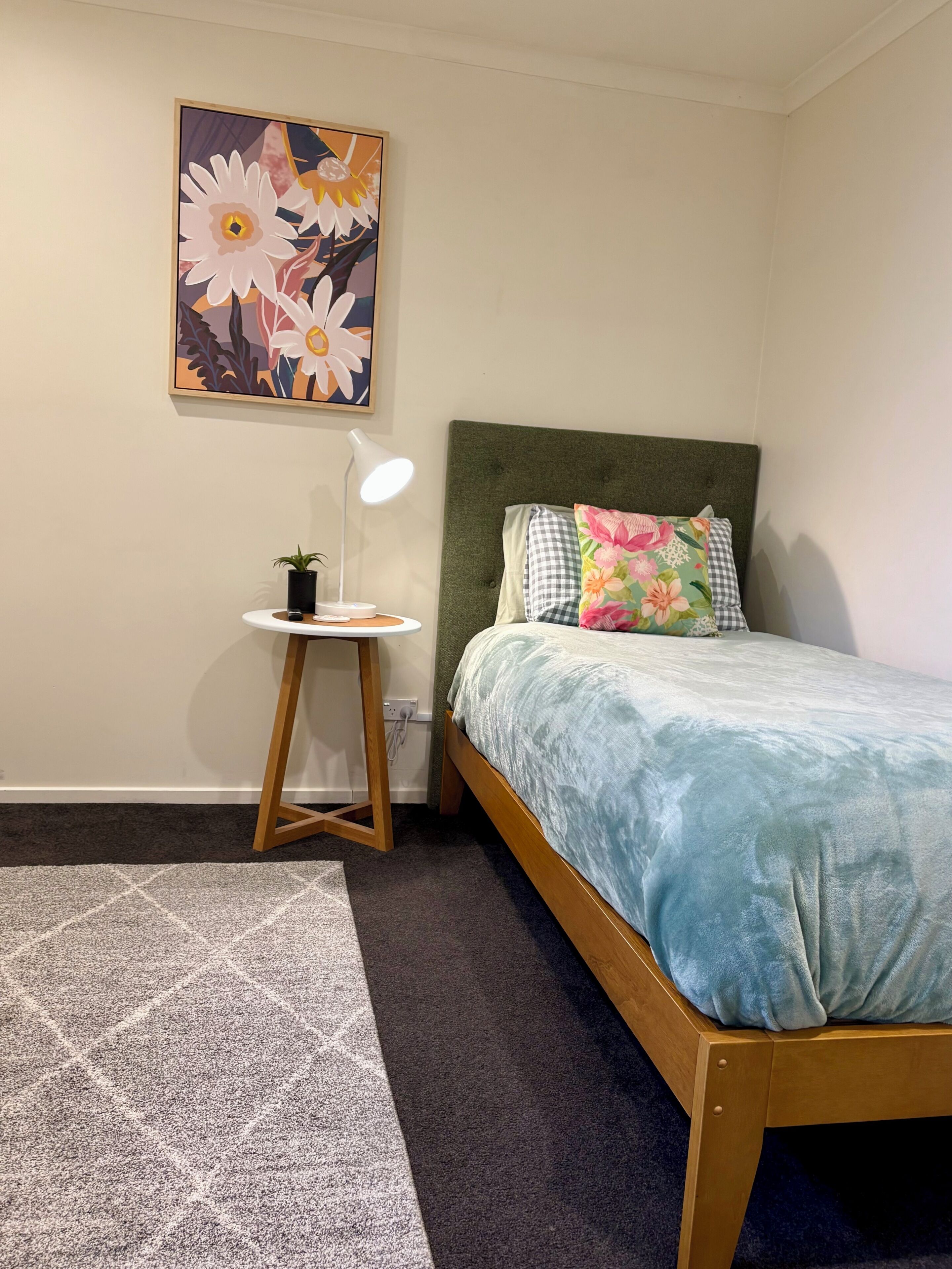 Une chambre à coucher avec un lit, une table de chevet avec une lampe, un tableau accroché au mur et un tapis à motifs.