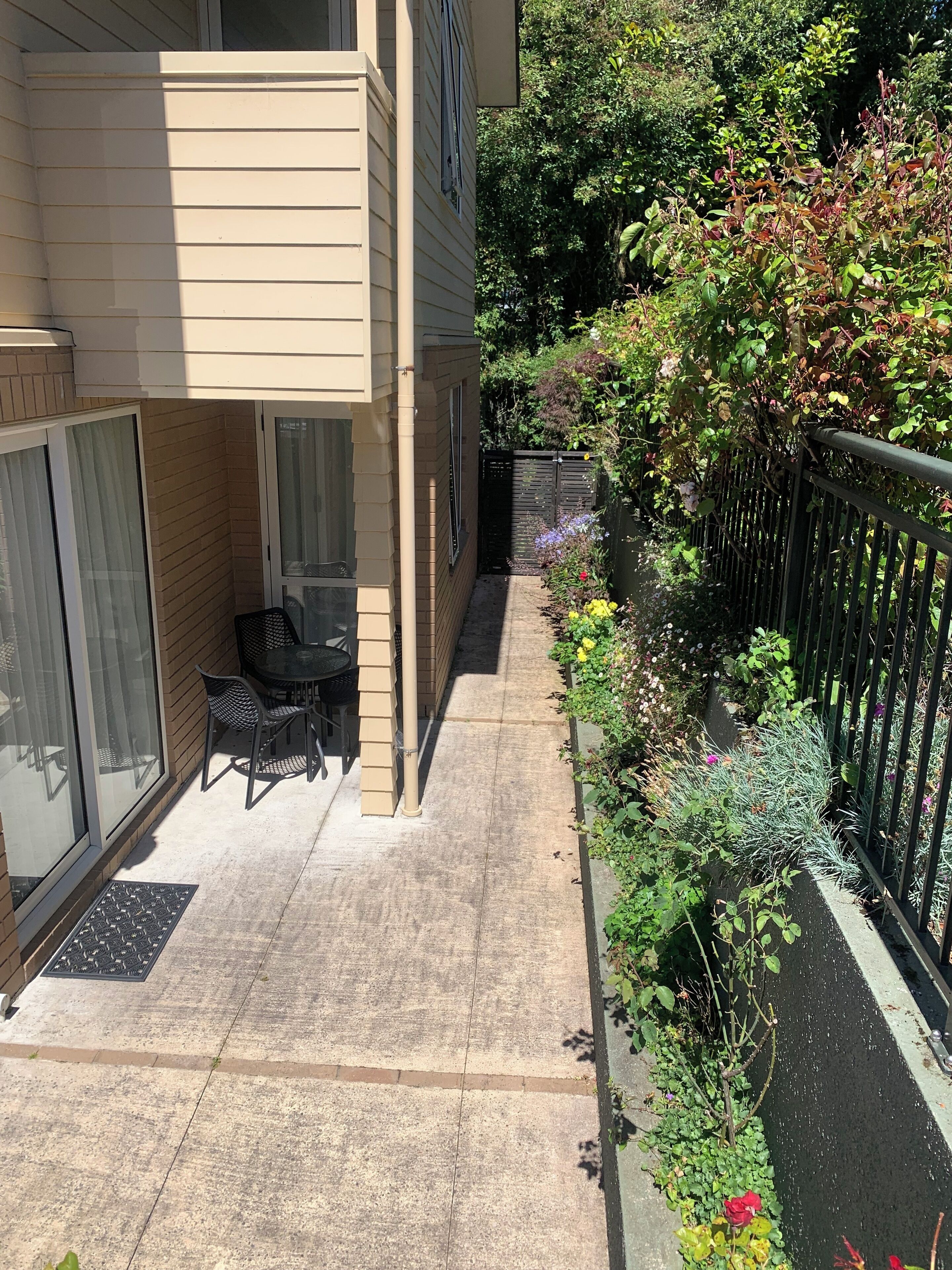 A balcony with a table and chairs, a black metal fence, and a variety of plants.