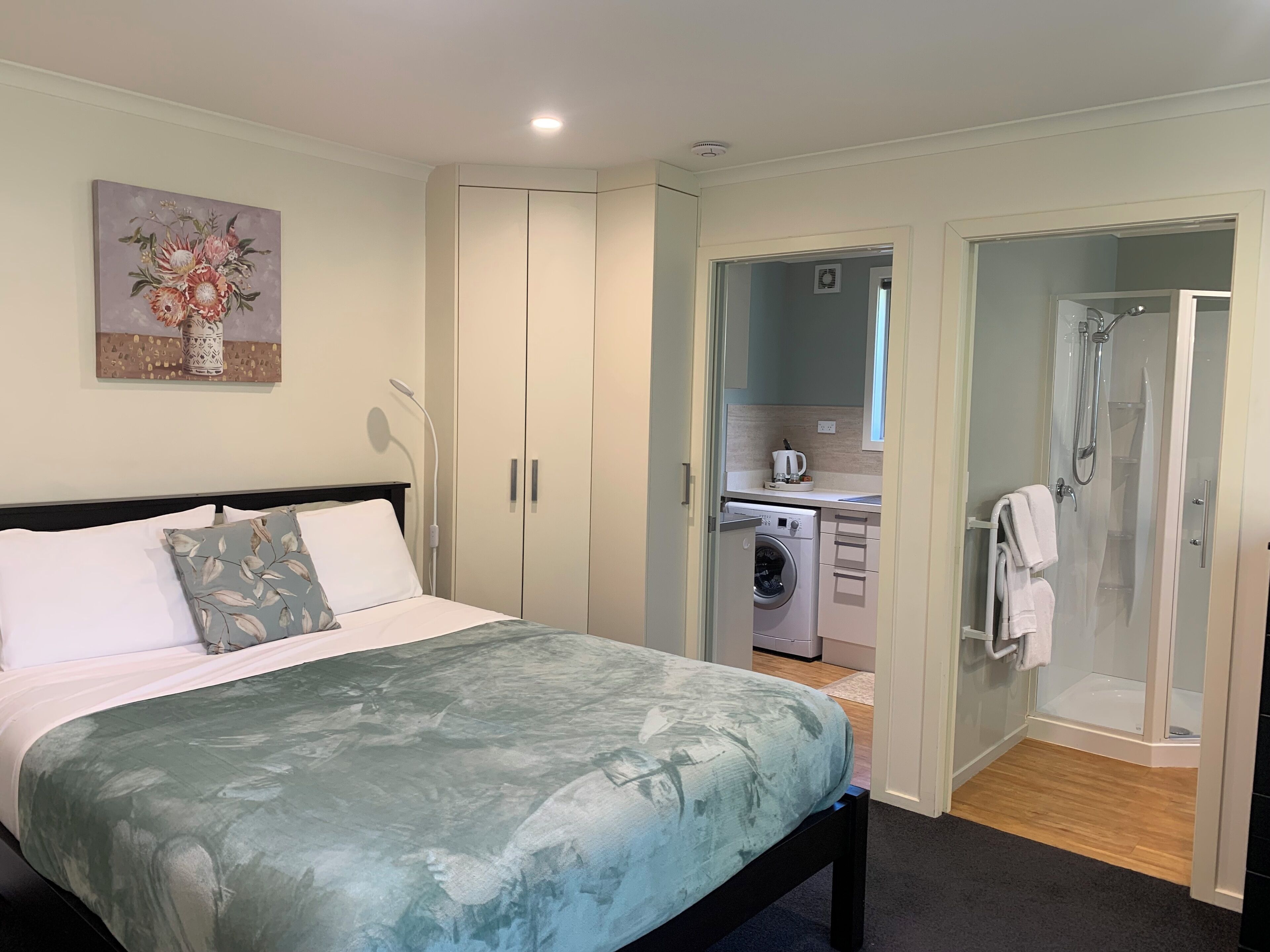 Un dormitorio con cama, lavadora, ducha y una pequeña kitchenette.