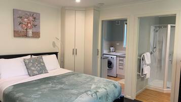 A bedroom with a bed, a washing machine, a shower, and a small kitchenette.