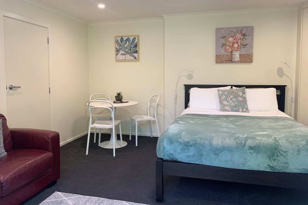 A bedroom with a bed, a desk with chairs, and a red sofa.