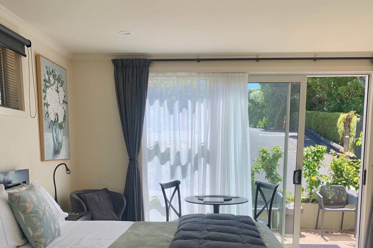 A bedroom with a bed, a chair, a table, and a view of the outside.