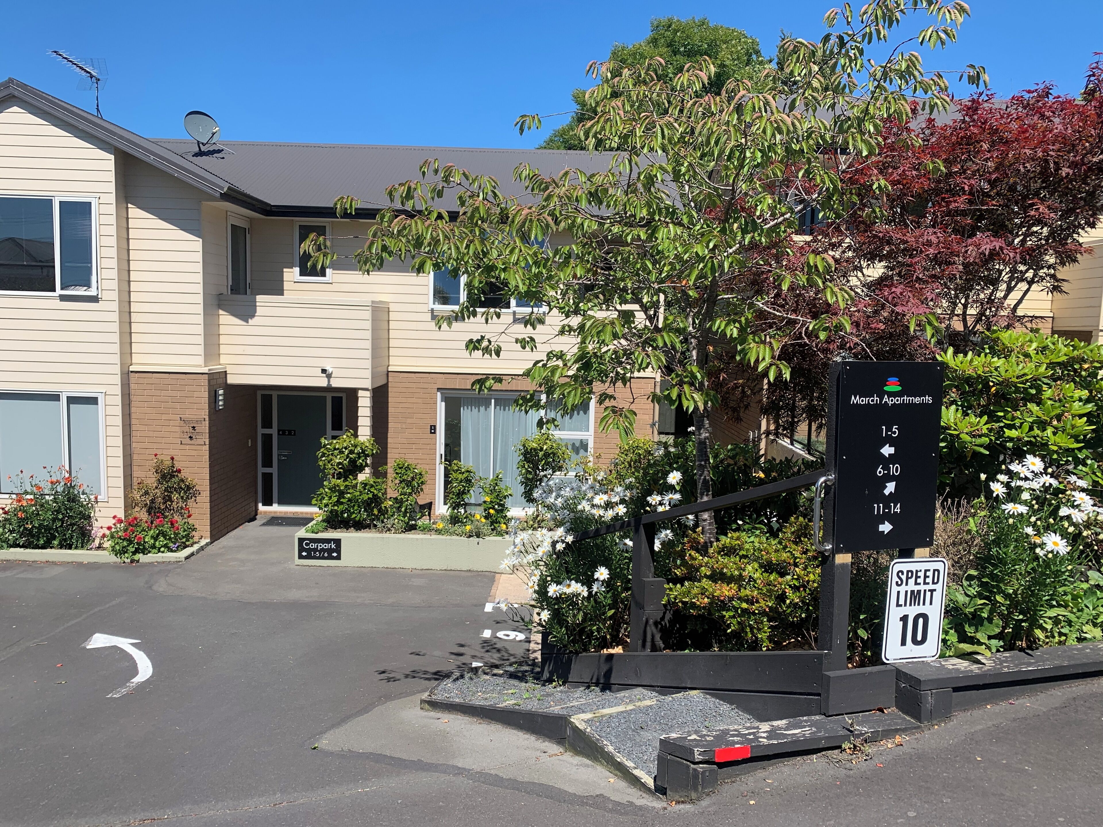 A residential building with a sign indicating March Apartments, with directional arrows for different apartment numbers. A speed limit sign of 10 is also visible.