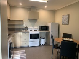 Cocina compacta con estufa, microondas, refrigerador y una pequeña zona de comedor con mesa y sillas.