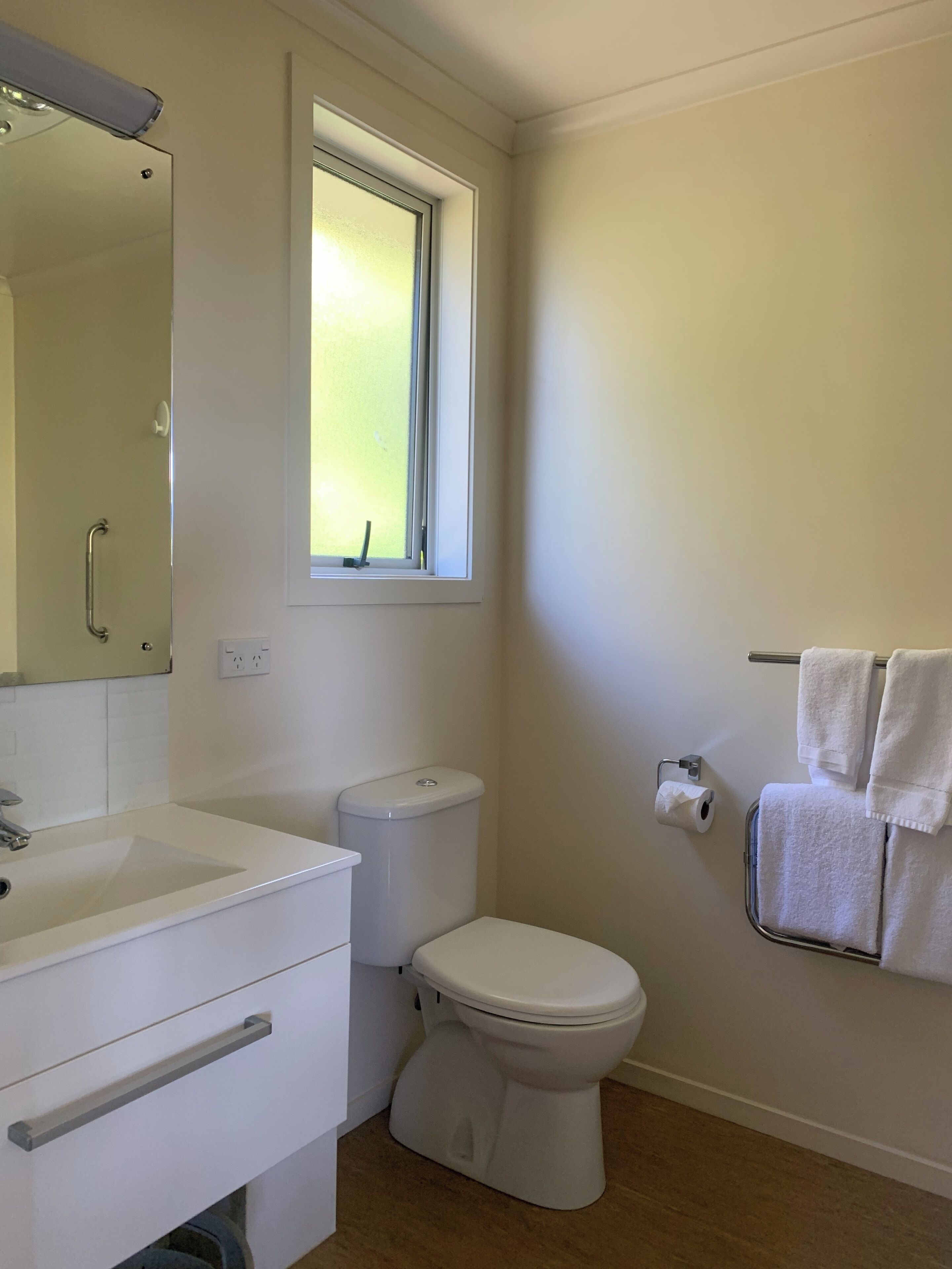 Un baño con lavamanos, inodoro y ventana blanca.