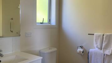 Un baño con lavamanos, inodoro y ventana blanca.