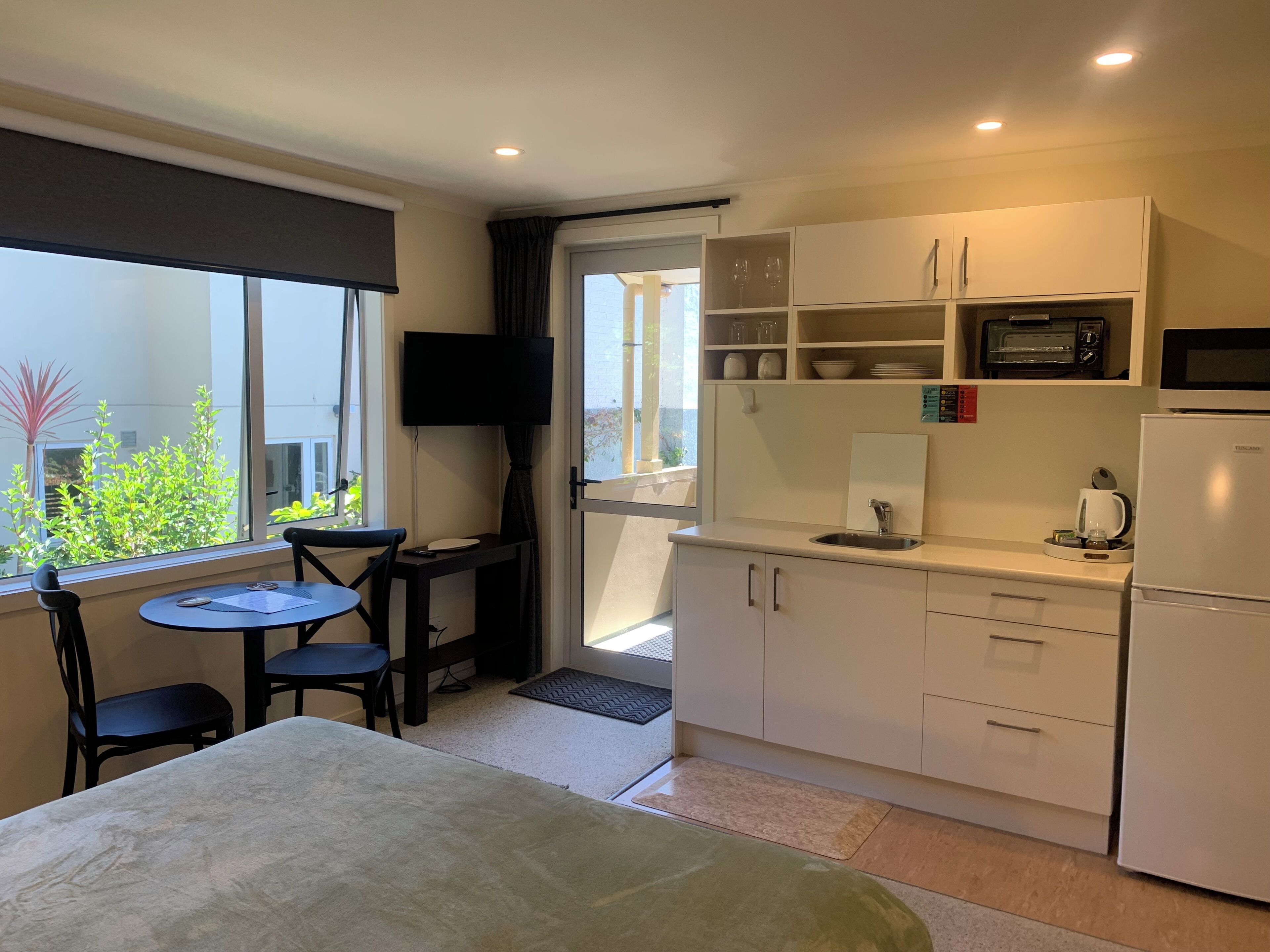 A compact kitchenette with a microwave, toaster, and sink. There is a small dining area with a table and chairs, and a TV mounted on the wall.