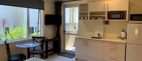 Una kitchenette compacta equipada con microondas, tostadora y lavaplatos. Hay un pequeño comedor con mesa y sillas, y un televisor montado en la pared.