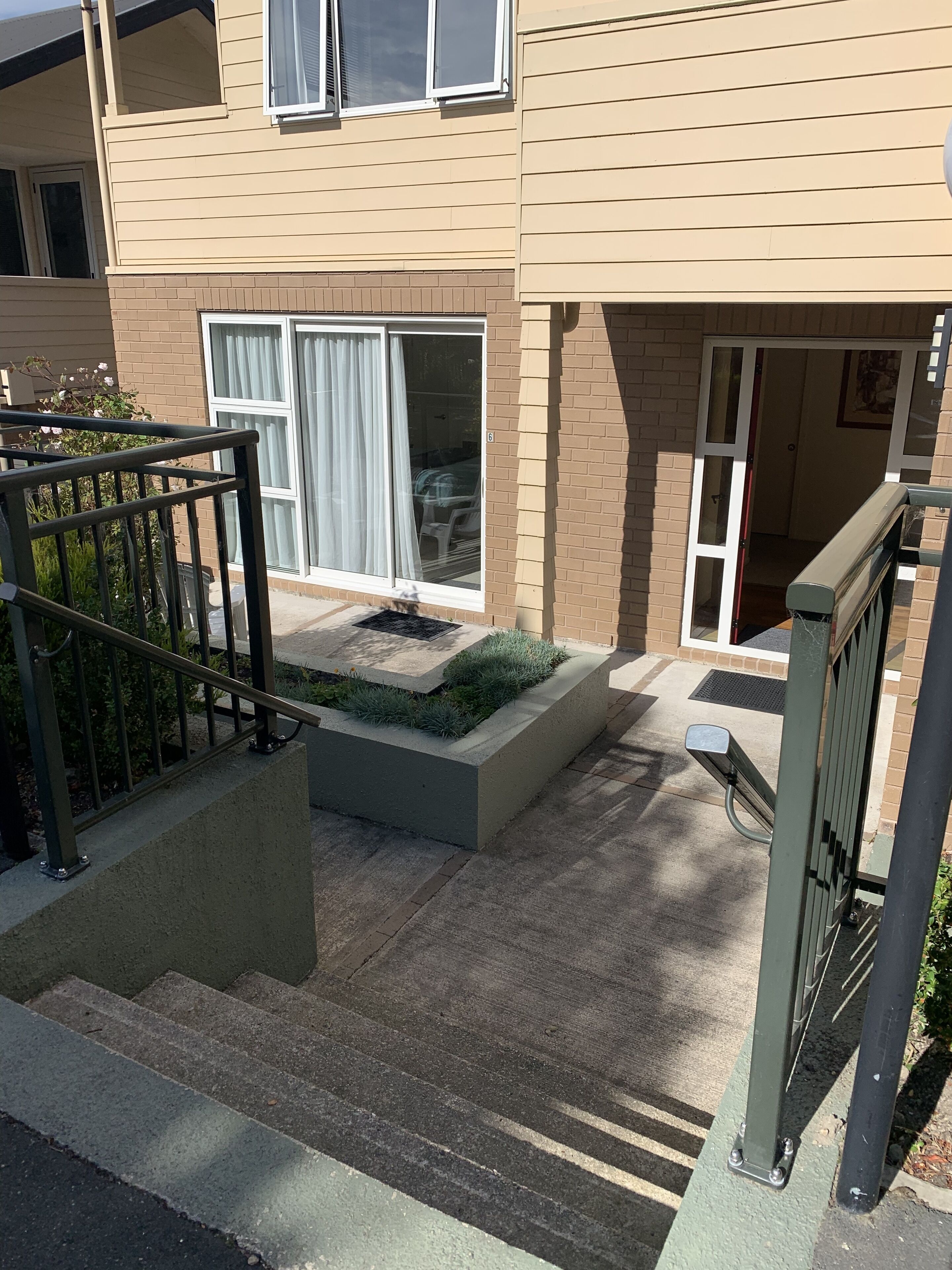 A residential building with a front entrance, a small garden area with a concrete planter, and a metal gate.