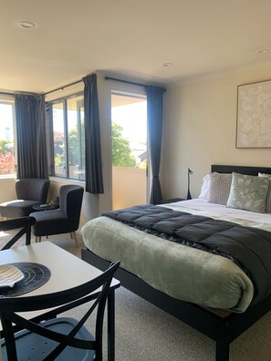 Una camera d'albergo con un letto, una scrivania e due sedie. C'è una finestra con tende e una pianta sulla scrivania.