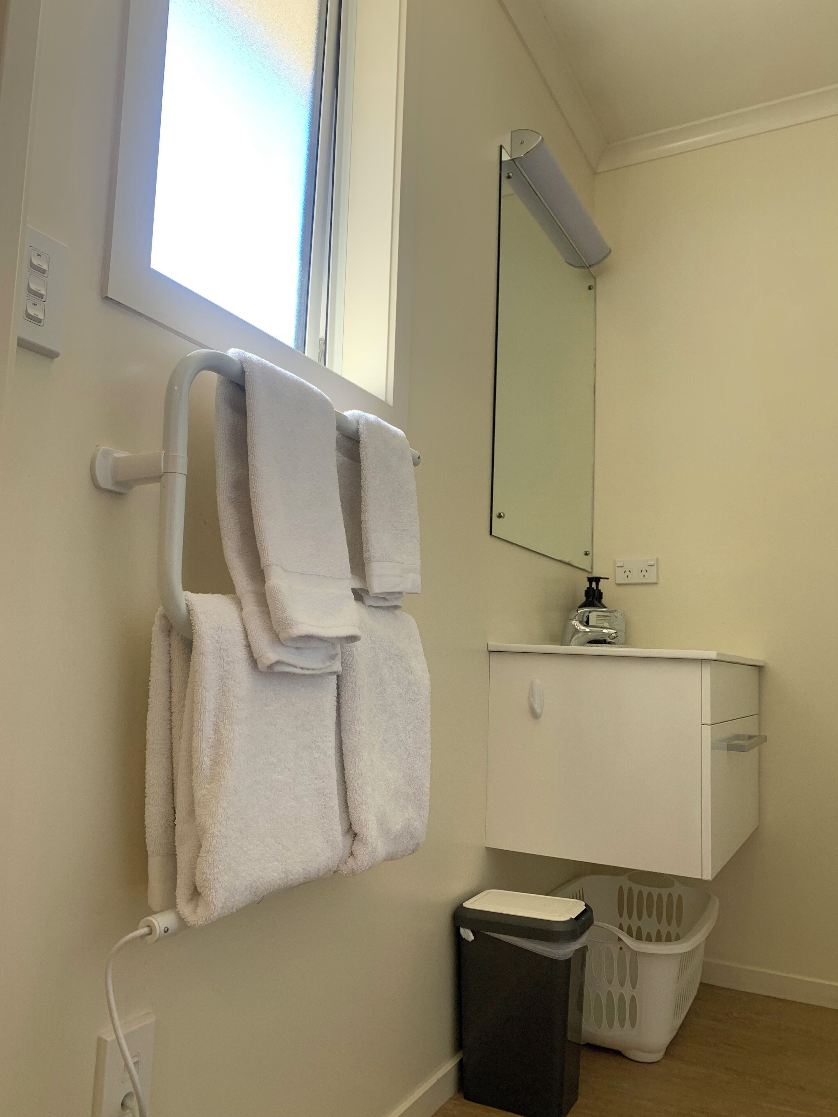 A bathroom with a towel rack holding two towels, a mirror, a sink, a trash bin, and a laundry basket.