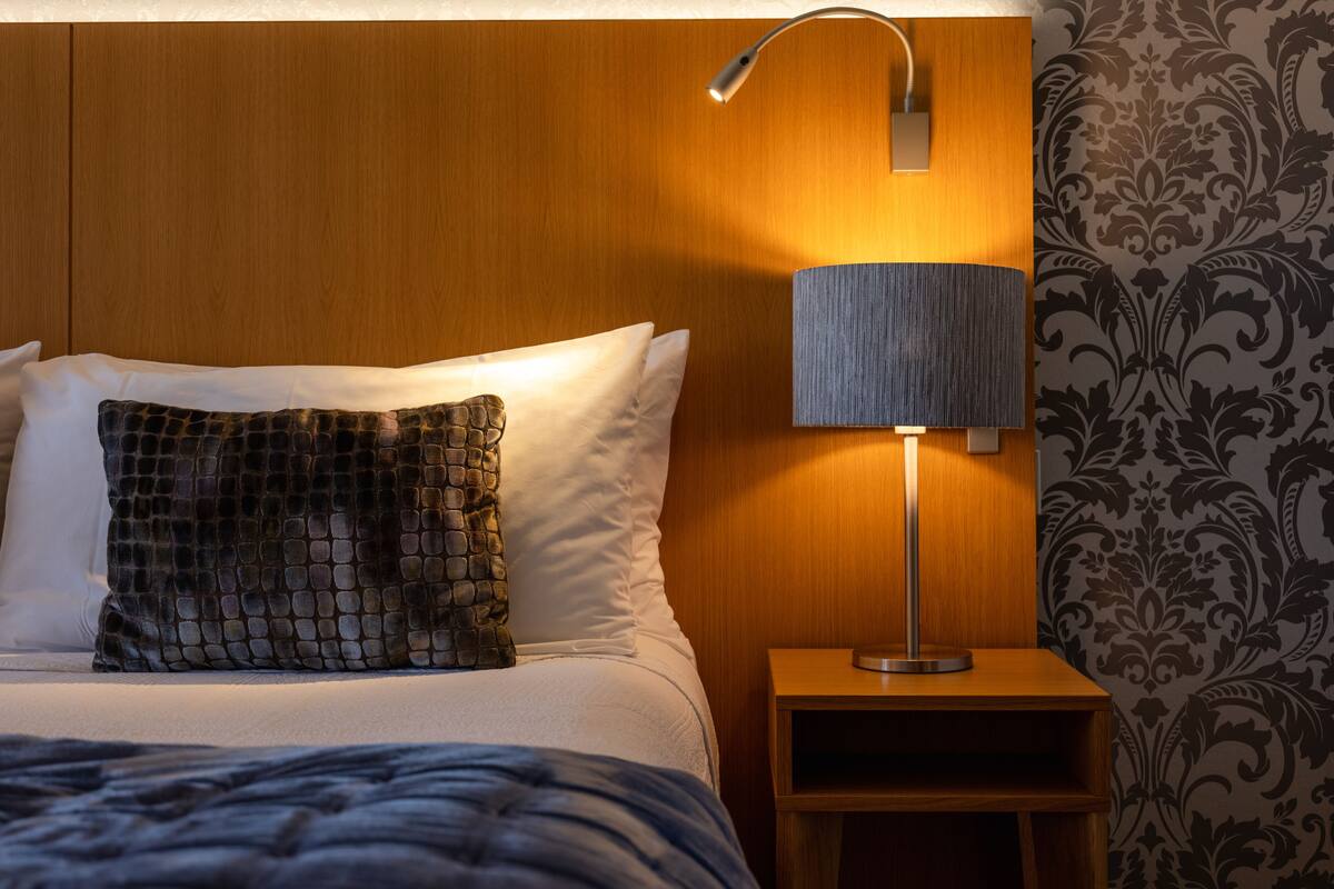 A neatly made bed with a patterned pillow and a bedside lamp on a wooden nightstand.