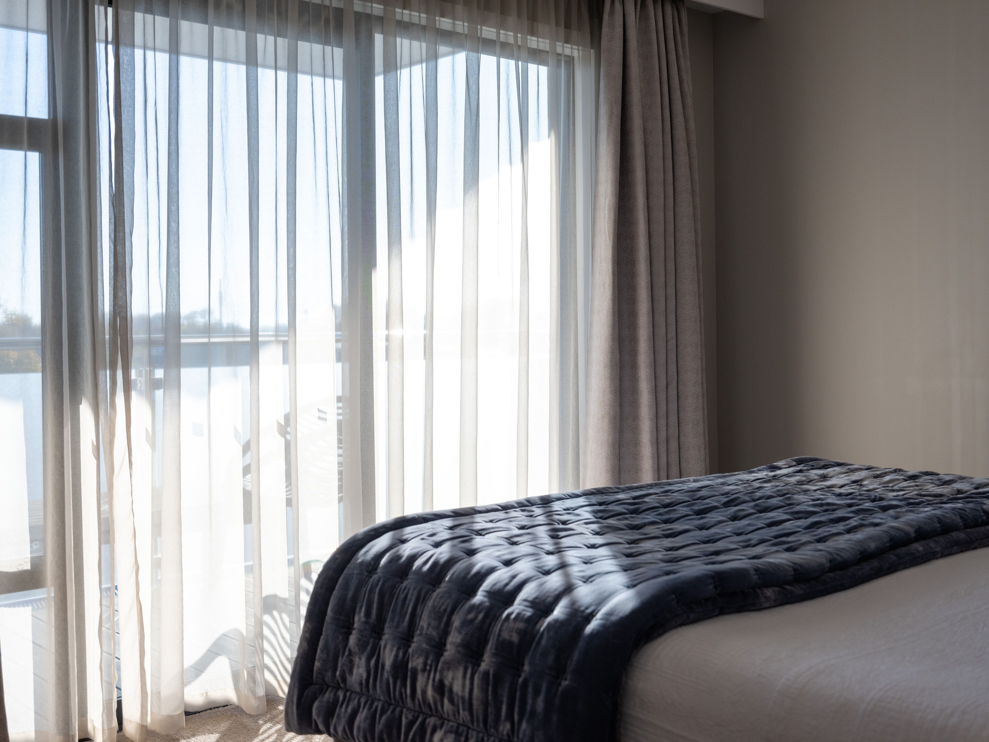 A bedroom with a bed, sheer curtains, and a view of a body of water.