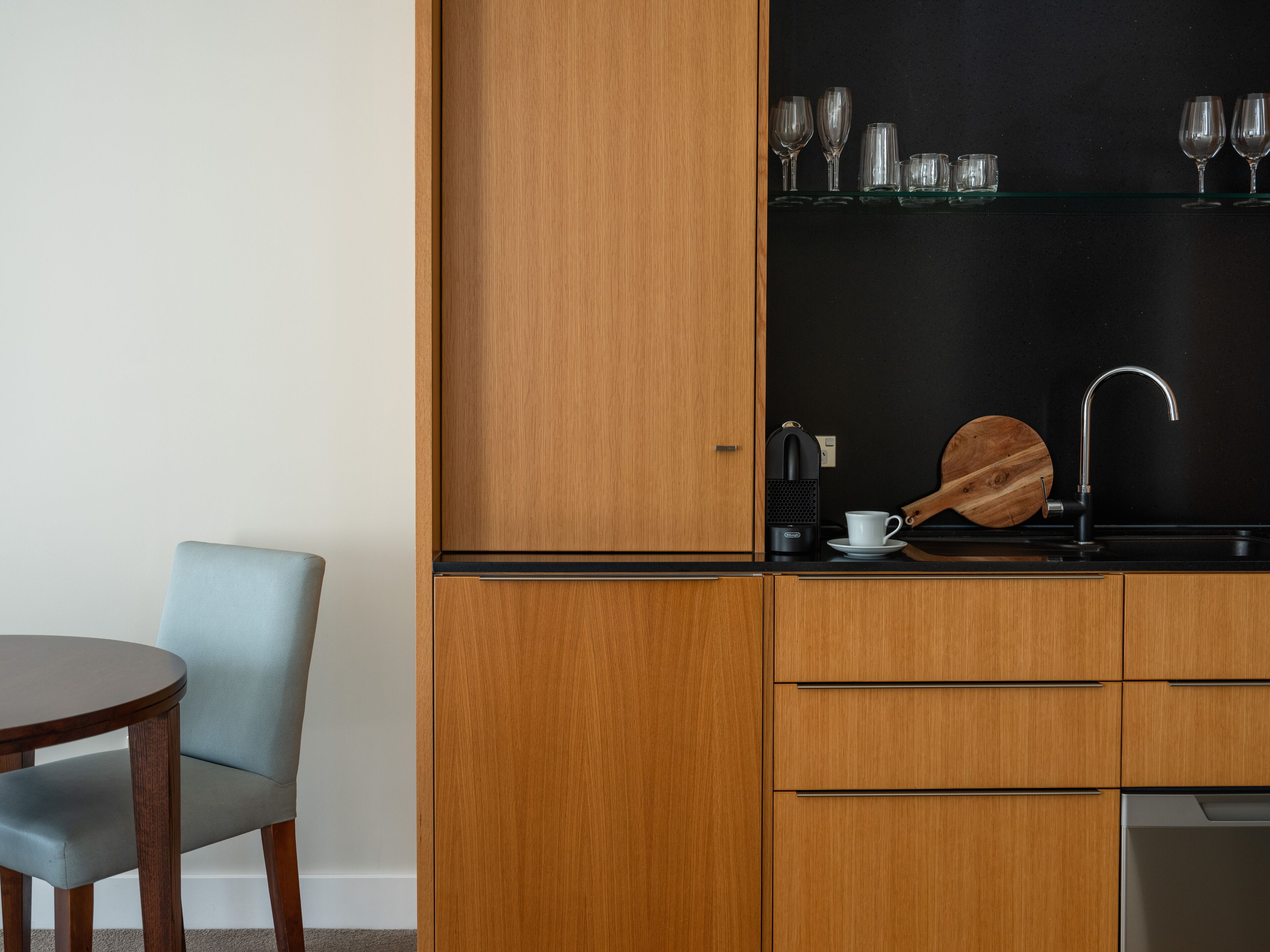 Una cocina compacta con armarios de madera, una encimera negra y una tabla de cortar redonda de madera.