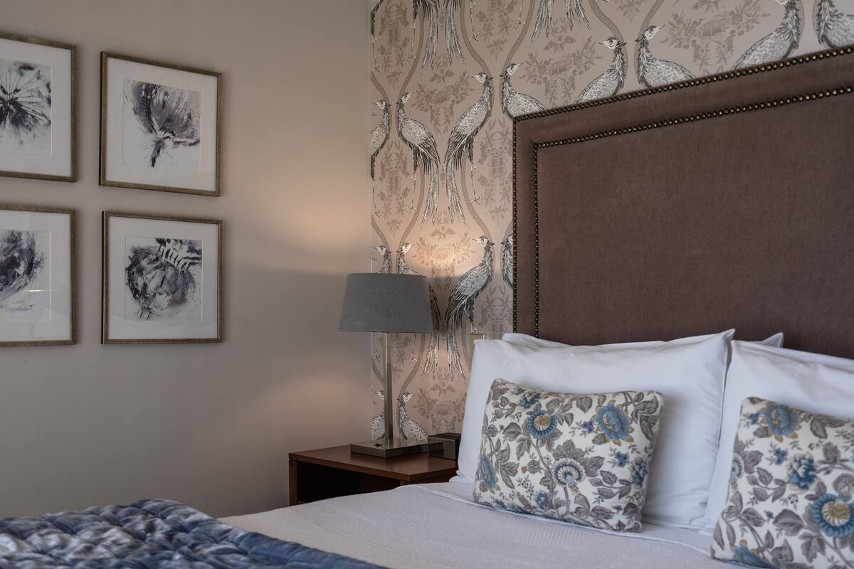 A neatly made bed with floral pillows, a bedside lamp, and framed artwork on the wall.