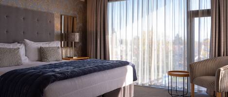 A hotel room with a large bed, a chair, a nightstand, and a window with curtains.