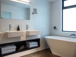 A modern bathroom with two sinks, a large bathtub, and a built-in shelf with towels. - Porters Boutique Hotel & Conference Centre (Havelock North)