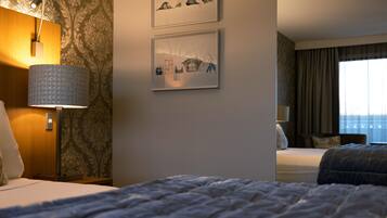Quarto de hotel com cama, escrivaninha, luminária e duas fotografias emolduradas na parede.