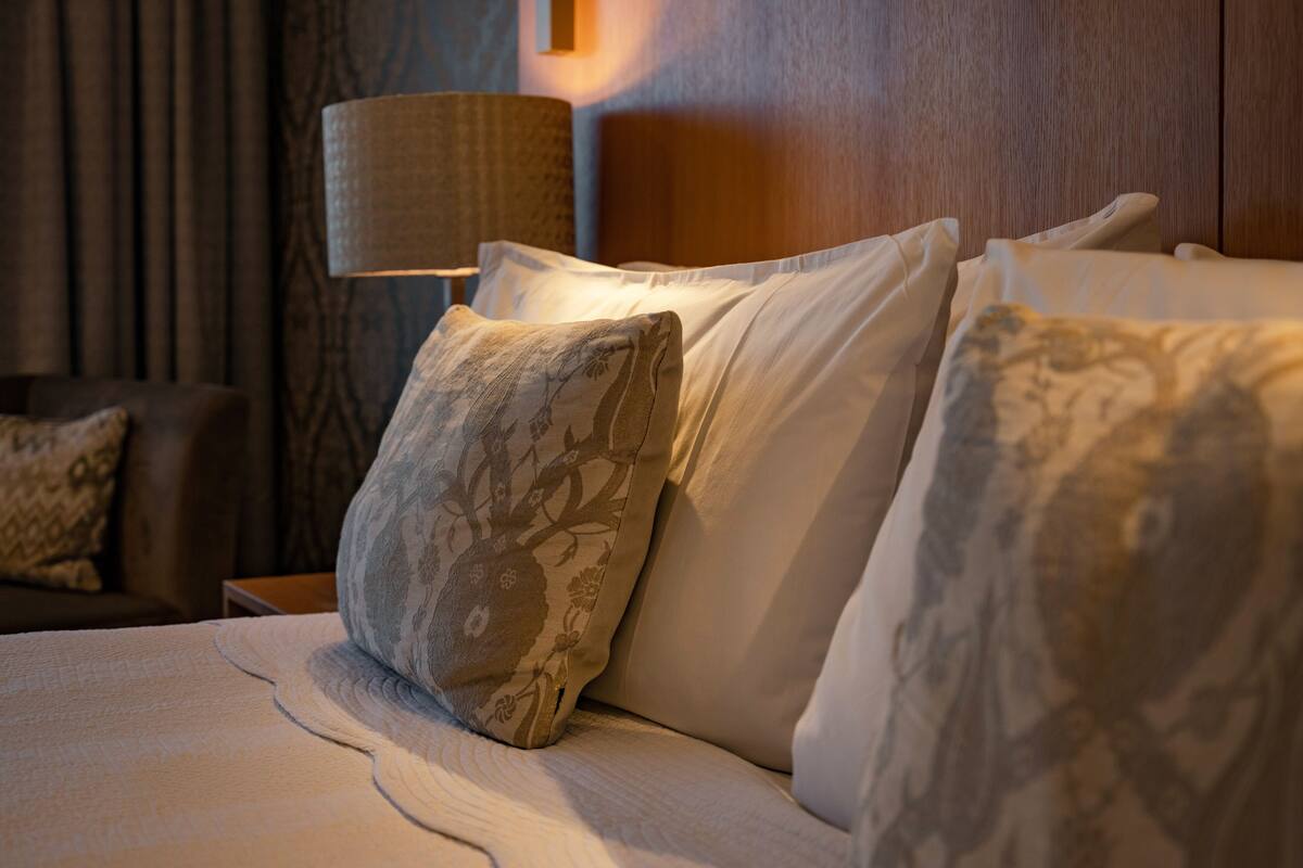 A neatly made bed with patterned pillows and a lamp on a wooden nightstand.