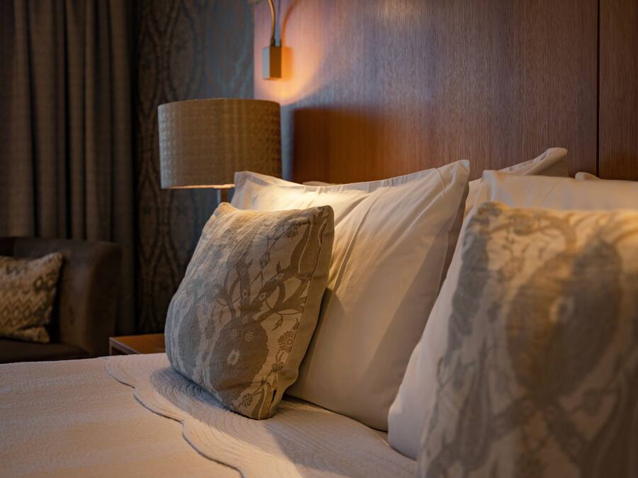 Una cama bien hecha con almohadas estampadas y una lámpara sobre una mesita de noche de madera.