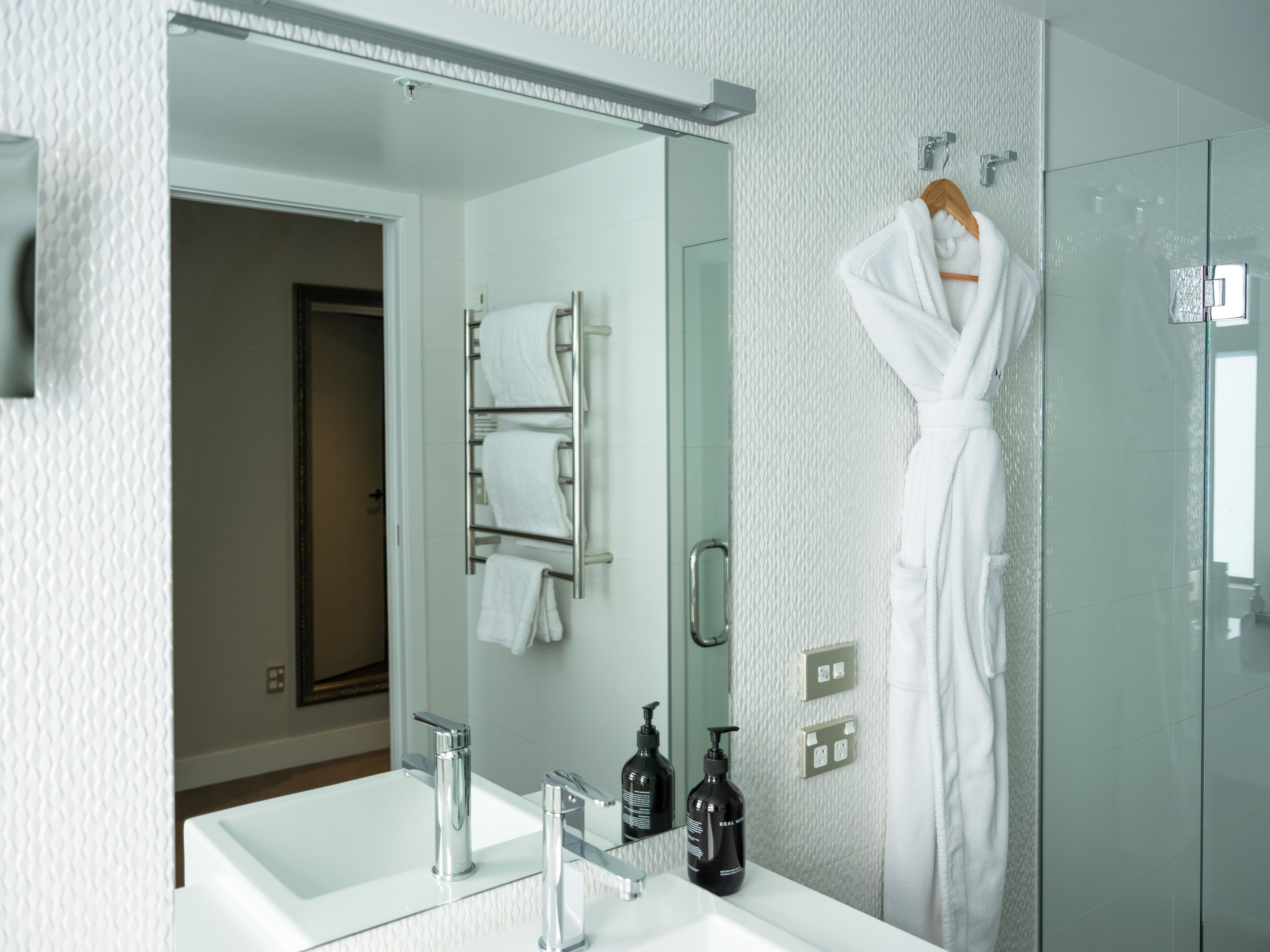 Ein modernes Badezimmer mit Duschkabine aus Glas, einem weißen Waschbecken mit Spiegel und einem Handtuchhalter mit weißen Handtüchern.