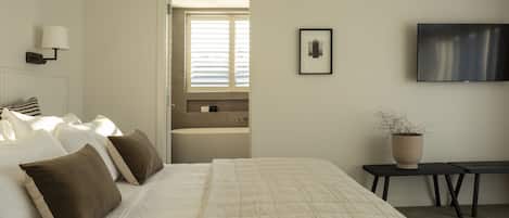 Habitación de hotel con una cama grande, televisión, una mesita y una planta en maceta.