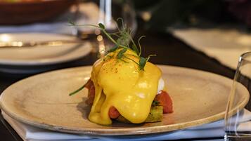 A plate with a dish that includes a poached egg, greens, and a slice of tomato, topped with a yellow sauce.