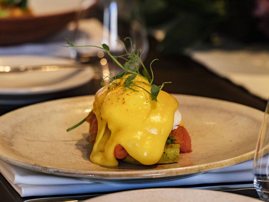 A plate with a dish that includes a poached egg, greens, and a slice of tomato, topped with a yellow sauce.