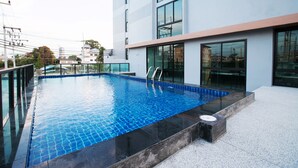 A modern swimming pool with clear blue water, surrounded by a glass barrier and a concrete edge.
