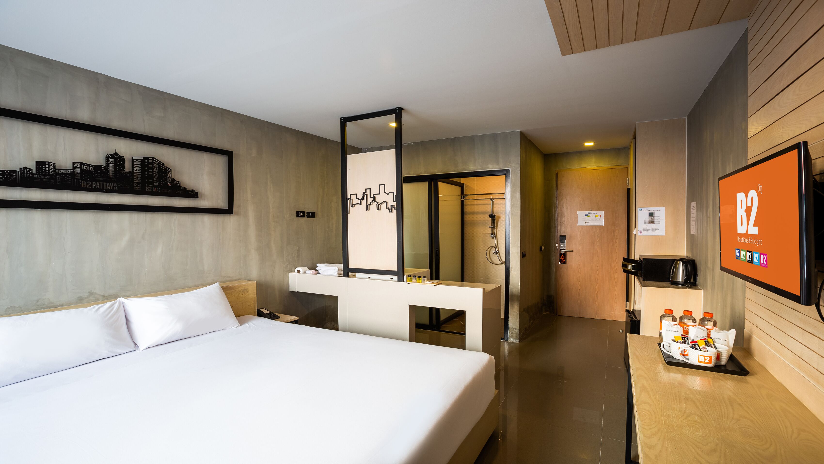 Habitación de hotel con cama, escritorio con espejo, baño con ducha y televisión mostrando 'B2 BoutiqueBudget'.
