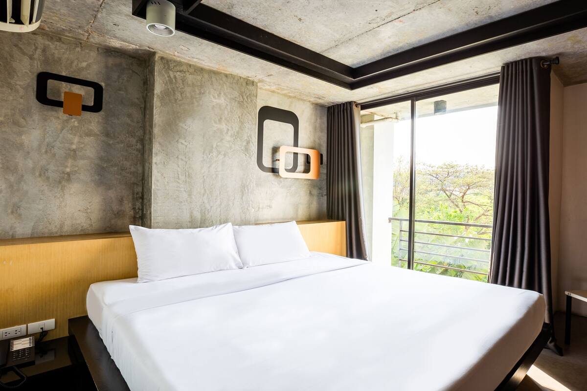 A hotel room with a large bed, a desk with a telephone, and a chair.