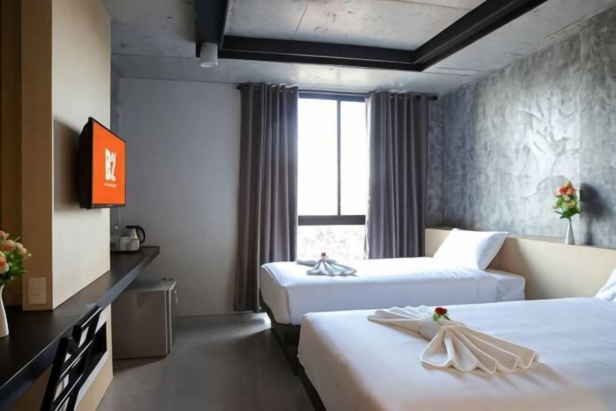 A hotel room with two beds, a flat-screen TV, a small kitchenette, and a large window with curtains.