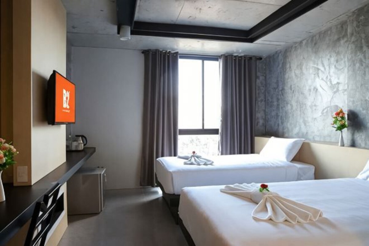 A hotel room with two beds, a flat-screen TV, a small kitchenette, and a large window with curtains.
