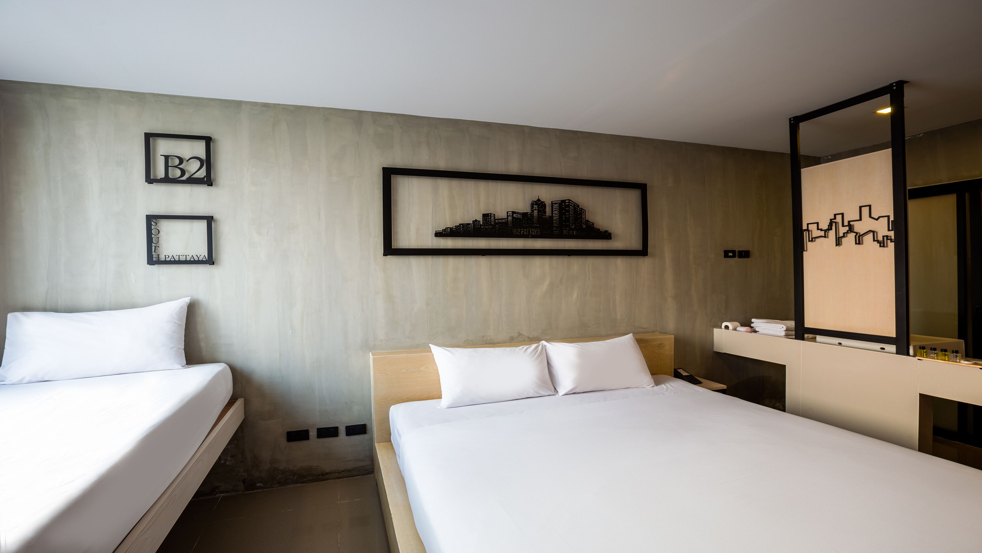 A hotel room with two beds, a cityscape wall art, a framed sign, and a mirror with a geometric design.