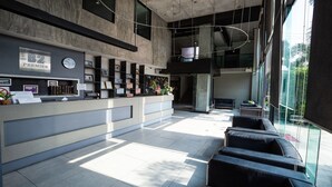 A modern reception area with a check-in desk, framed pictures, and a clock. There are seating areas with a view of the outdoors.