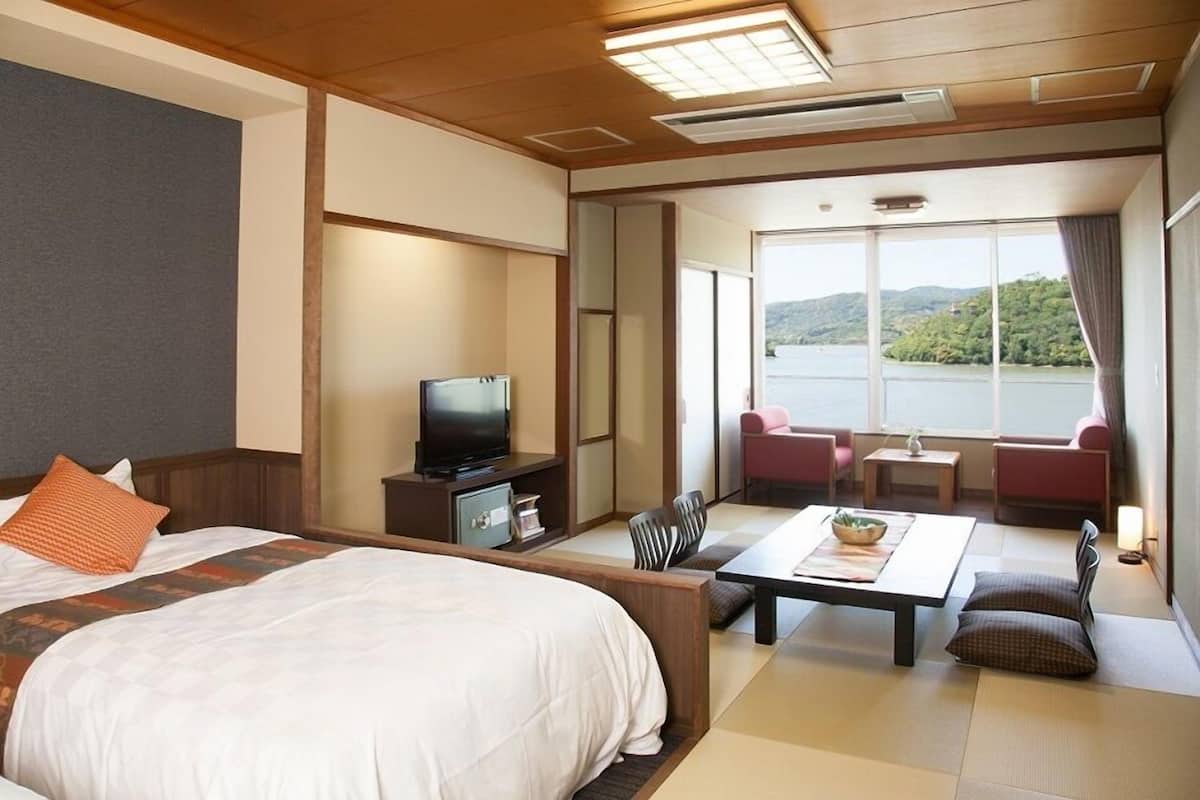 A hotel room with a bed, a television, a seating area with a table, and a view of a lake.