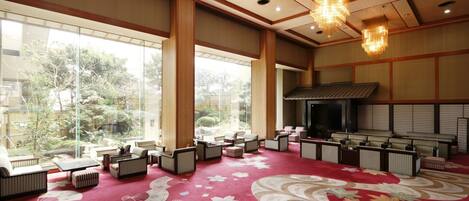 A spacious room with large windows, a red carpet with floral patterns, and a traditional-style ceiling with wooden beams and a hanging chandelier.