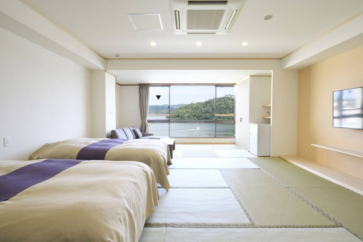 A hotel room with two beds, a view of a body of water, and a balcony.